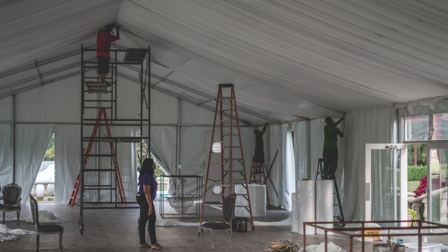 Event professionals work on interior decorations inside a large tent.