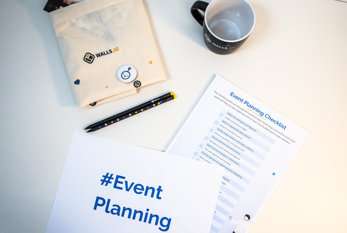 Event planning checklist and branded items on a white desk.